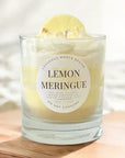 Lemon meringue candle in a glass jar with a decorative label on a wooden surface.