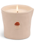A lit ceramic candle in a beige container with a hand-painted mushroom design on the front, displayed against a white background.