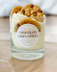 Candle labeled 'Chocolate Chip Cookies' with cookies on top, on a wooden surface.