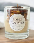 Candle labeled 'Maple Pancakes' with a decorative design on a wooden surface.