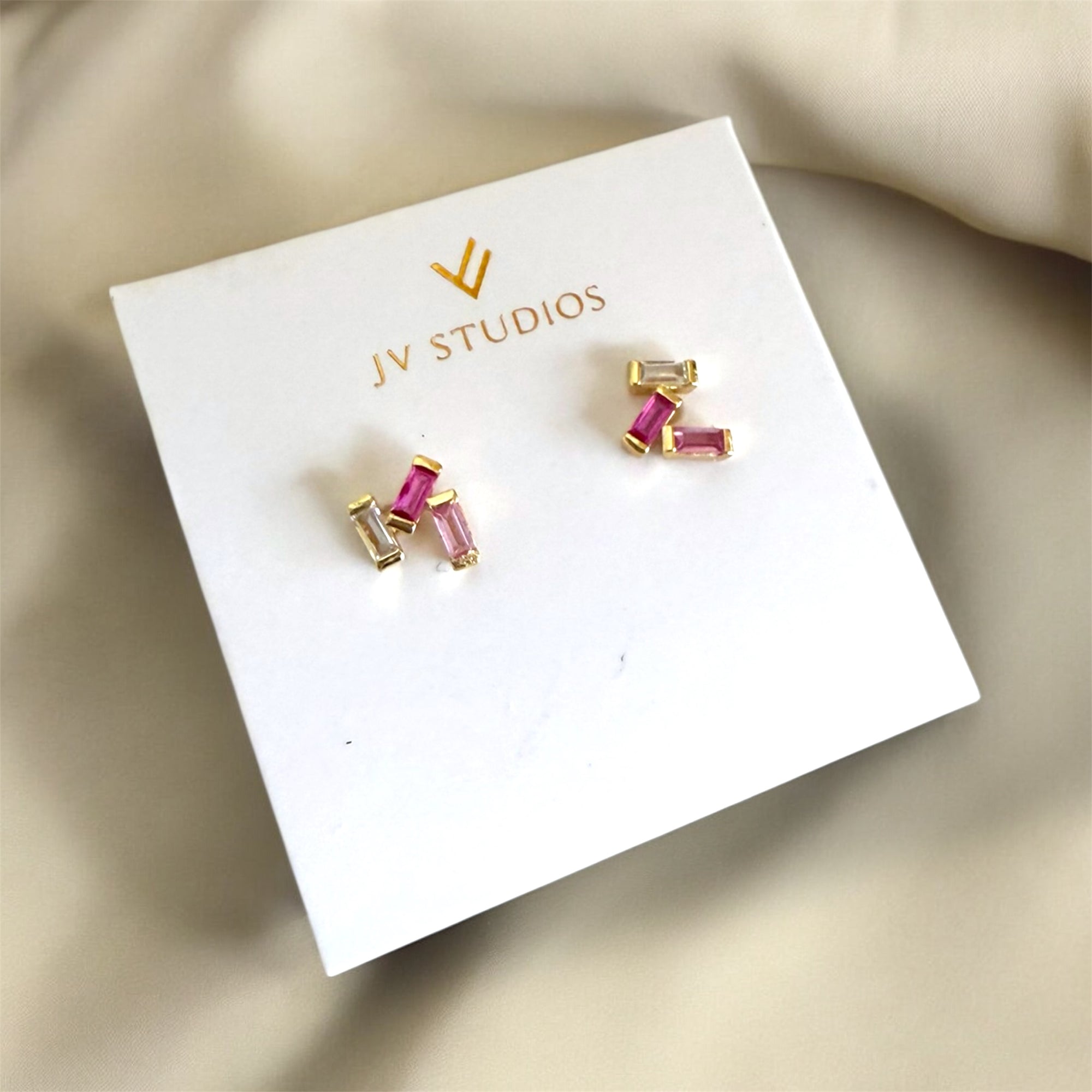 Gold and pink stud earrings on a JV Studios branded card.
