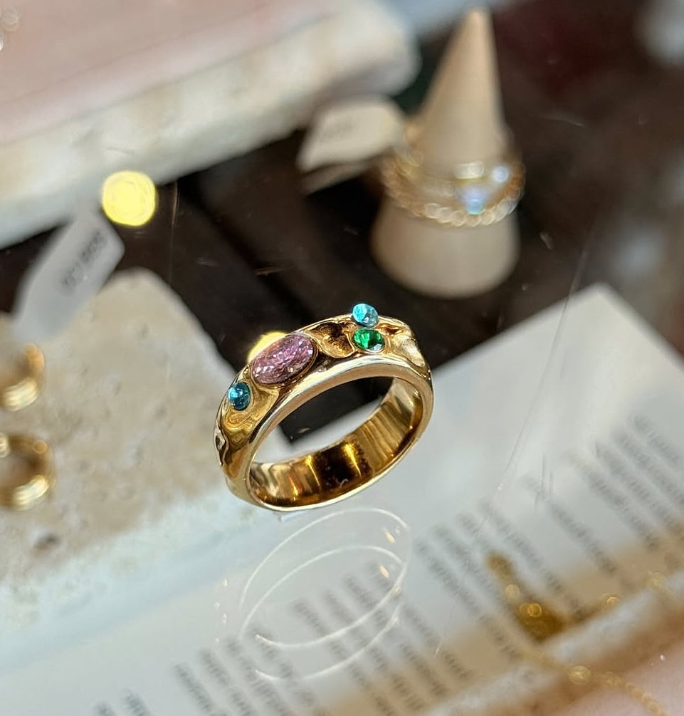 Gold ring with colorful gemstones on a textured surface