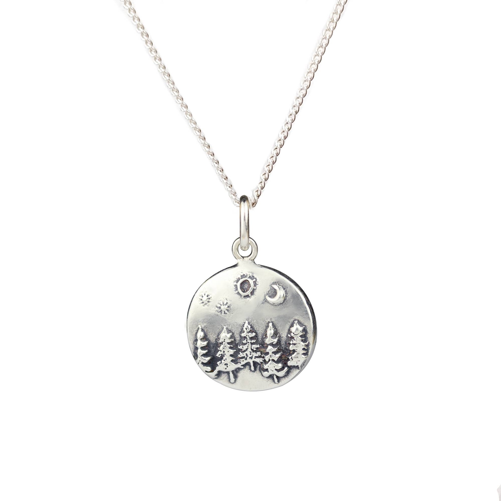 Silver necklace with a round pendant featuring trees and celestial elements on a white background