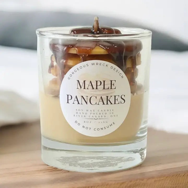 Candle labeled 'Maple Pancakes' with a decorative design on a wooden surface.